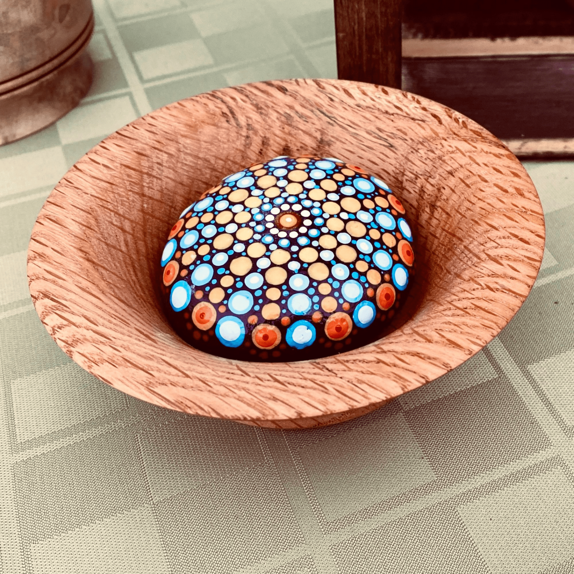 A colorful painted rock with intricate dot patterns inside a wooden bowl on a checkered tablecloth A colorful painted rock with intricate dot patterns inside a wooden bowl on a checkered tablecloth